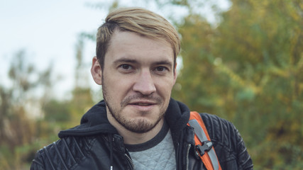 A handsome guy posing against the autumn nature. Blond in a leather jacket on the street