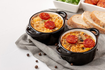 Slovak Christmas cabbage soup in two small pots with sausage on top on white background.