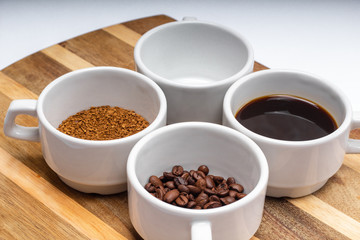 assortment of four white cups of coffee on a saucer grain, instant, brewed and an empty cup on the wooden surface background