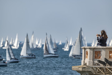 Obraz premium Donna giovane che fotografa con cellulare una regata velica con tante barche a vela