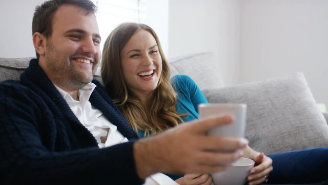 Young caucasian couple relax on their couch with hot drinks watching television