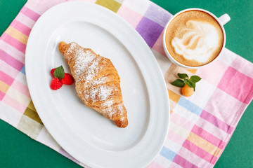 Fresh homemade croissants and coffee on cloth napkin decorated with raspberry. Top view with copy space on green background