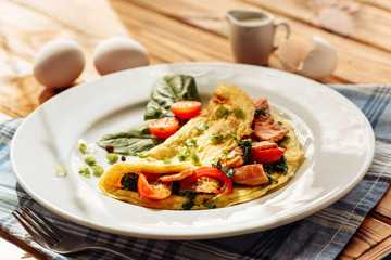 Herb omelette with chives, cherry tomatoes and spinach on wooden table under sunlight. Healthy breakfast concept