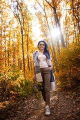 young pretty casual woman in the forest. gold autumn. female is looking up. girl is walking in the sunny park. lifestyle concept