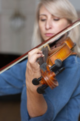 Young beautiful woman violin player looking at camera over instrument on her shoulder holding bow.
