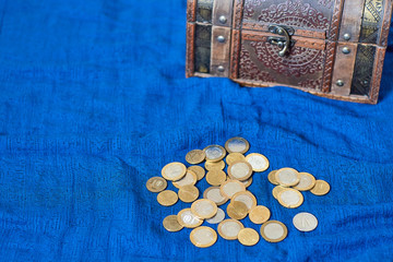 Currency money coins of different countries lie on a blue background next to a wooden brown antique...