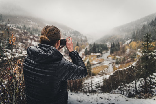 A man taking a photo in the mountains during an autumn snow storm. 