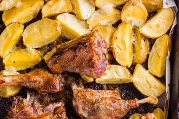 Baked meat with potatoes. Duck meat with golden crust on baking sheet. Cooked in oven dish on parchment. Golden sliced potatoes with chicken meat. Home kitchen