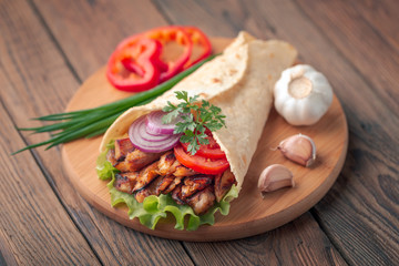 Doner kebab is lying on the cutting board. Shawarma with chicken meat, onions, salad lies on a dark old wooden table.