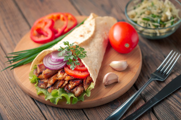 Doner kebab is lying on the cutting board. Shawarma with chicken meat, onions, salad lies on a dark old wooden table.