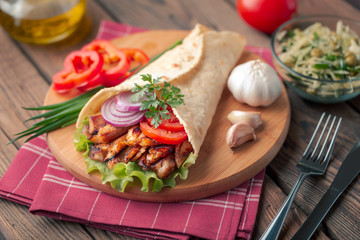 Doner kebab is lying on the cutting board. Shawarma with chicken meat, onions, salad lies on a dark old wooden table.