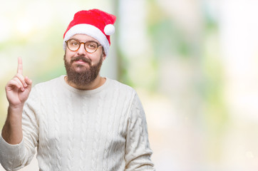 Young caucasian man wearing christmas hat and glasses over isolated background pointing finger up with successful idea. Exited and happy. Number one.