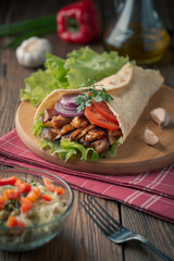 Doner kebab is lying on the cutting board. Shawarma with chicken meat, onions, salad lies on a dark old wooden table.