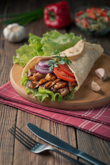 Doner kebab is lying on the cutting board. Shawarma with chicken meat, onions, salad lies on a dark old wooden table.