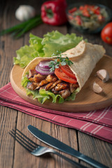 Doner kebab is lying on the cutting board. Shawarma with chicken meat, onions, salad lies on a dark old wooden table.