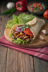 Doner kebab is lying on the cutting board. Shawarma with chicken meat, onions, salad lies on a dark old wooden table.