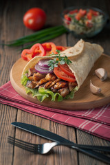 Doner kebab is lying on the cutting board. Shawarma with chicken meat, onions, salad lies on a dark old wooden table.