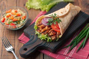 Doner kebab is lying on the cutting board. Shawarma with chicken meat, onions, salad lies on a dark old wooden table.