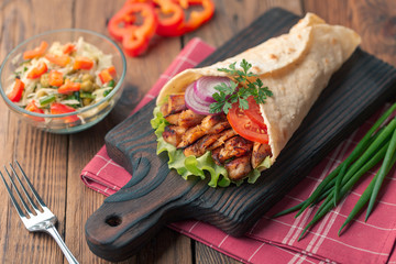 Doner kebab is lying on the cutting board. Shawarma with chicken meat, onions, salad lies on a dark old wooden table.