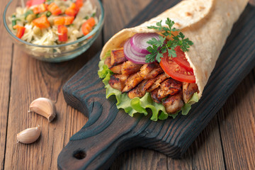 Doner kebab is lying on the cutting board. Shawarma with chicken meat, onions, salad lies on a dark old wooden table.