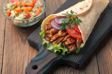 Doner kebab is lying on the cutting board. Shawarma with chicken meat, onions, salad lies on a dark old wooden table.