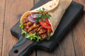 Doner kebab is lying on the cutting board. Shawarma with chicken meat, onions, salad lies on a dark old wooden table.