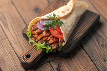Doner kebab is lying on the cutting board. Shawarma with chicken meat, onions, salad lies on a dark old wooden table.