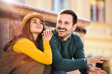Portrait of beautiful smiling love couple sitting near fountain outdoors in the city. Handsome young man and woman.