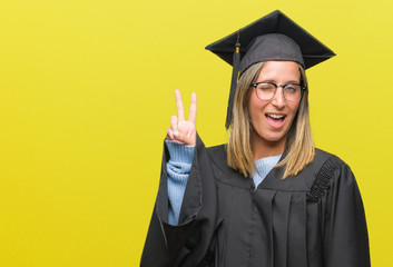 Young beautiful woman wearing graduated uniform over isolated background smiling with happy face winking at the camera doing victory sign. Number two.