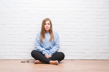 Young adult woman sitting on the floor in autumn over white brick wall skeptic and nervous, frowning upset because of problem. Negative person.