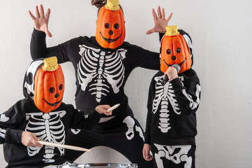 Happy friendly family of musicians in carnival costumes, boys and young mother play drum and try to sing with microphone. Black suit with image of skeletons. Classic halloween costume. Funny children