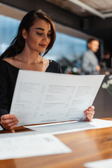 Young beautiful woman looking at menu deciding what to order in modern cafe.