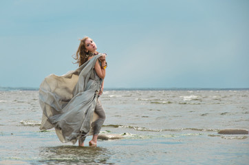 elf or fairy walks among the summer grasses in a grey dress swollen in the wind