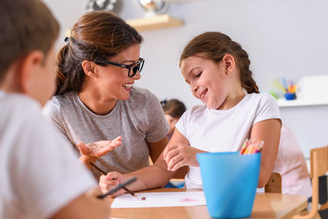 Preschool teacher looking at smart child learning to write and draw. Early education. Harnessing...