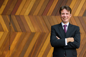Happy businessman smiling with arms crossed against zigzag patte