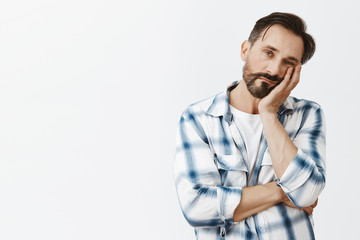 So boring. Indifferent cute adult man with beard and dark hair, leaning face on palm and gazing with careless tired expression at camera, fed up of listening meeting for hours, bored and exhausted