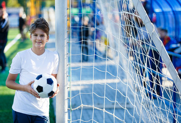 cute young boy in white blue sportswear holds classical black and white football ball on the green...