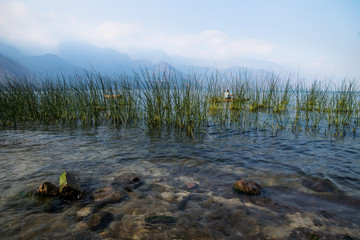 Boat behind reed with misty volcanic mountains at Lago Atitlan, San Juan la Laguna, Guatemala, Central America