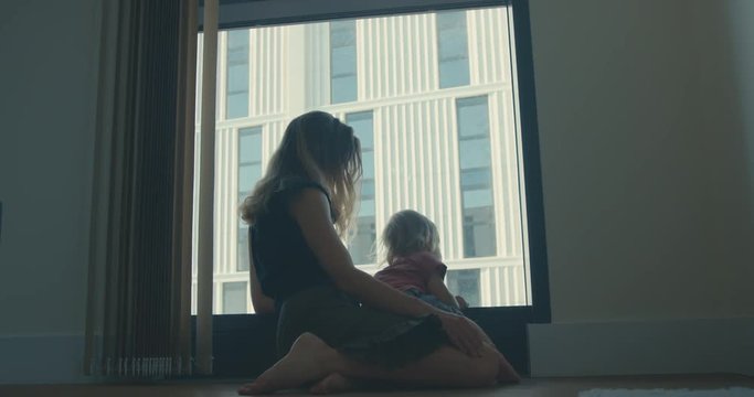 Mother and toddler sitting by window of high rise
