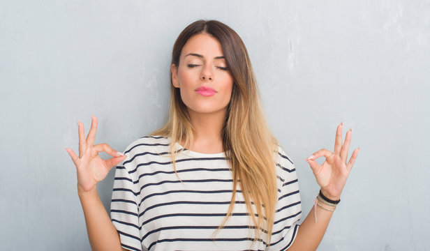 Young adult woman over grunge grey wall wearing navy t-shirt relax and smiling with eyes closed doing meditation gesture with fingers. Yoga concept.