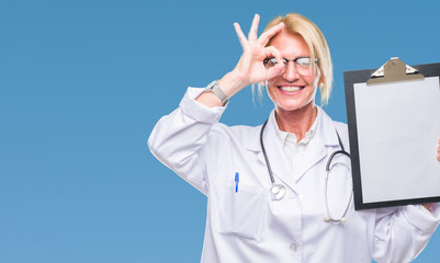 Middle age blonde doctor woman holding clipboard over isolated background with happy face smiling doing ok sign with hand on eye looking through fingers