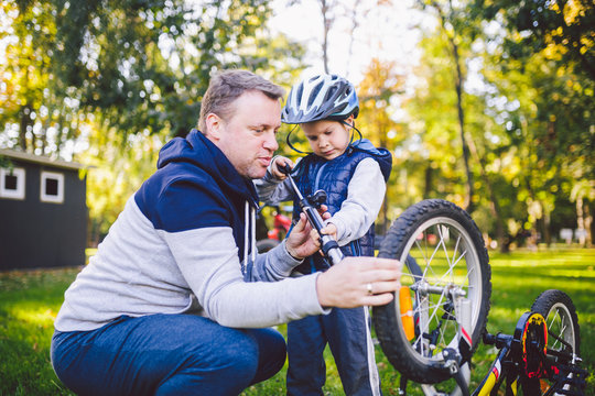 Father's day Caucasian dad and 5 year old son in the backyard near the house on the green grass on the lawn repairing a bicycle, pumping a bicycle wheel. Dad teaches how to repair a child's bike