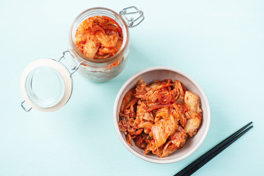 Kimchi cabbage in a bowl and jar with chopsticks on color background, Korean food