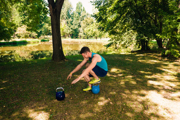 Sporty man exercise legs on kettlebell into the park