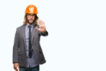 Young handsome architec man with long hair wearing safety helmet over isolated background doing stop sing with palm of the hand. Warning expression with negative and serious gesture on the face.