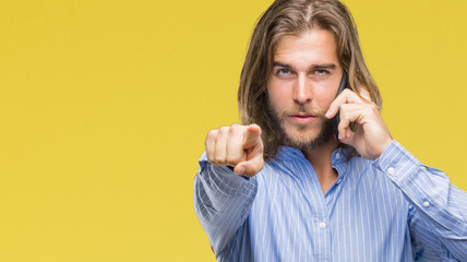 Young handsome man with long hair over isolated background talking on the phone pointing with finger to the camera and to you, hand sign, positive and confident gesture from the front