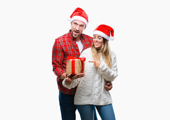 Young couple in love wearing christmas hat and holding present over isolated background very happy pointing with hand and finger