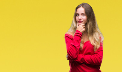 Fototapeta premium Young beautiful blonde woman wearing red sweater over isolated background looking confident at the camera with smile with crossed arms and hand raised on chin. Thinking positive.