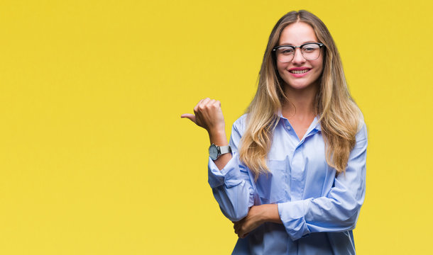 Young beautiful blonde business woman wearing glasses over isolated background smiling with happy face looking and pointing to the side with thumb up.
