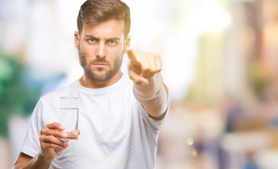 Young handsome man drinking glass of water over isolated background pointing with finger to the...